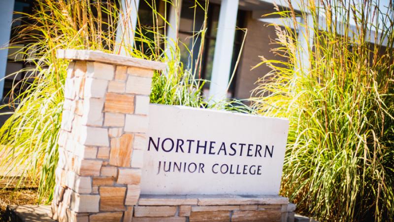 Northeastern Junior College Sign with building in background and tall ornamental grass on the sides of the sign.