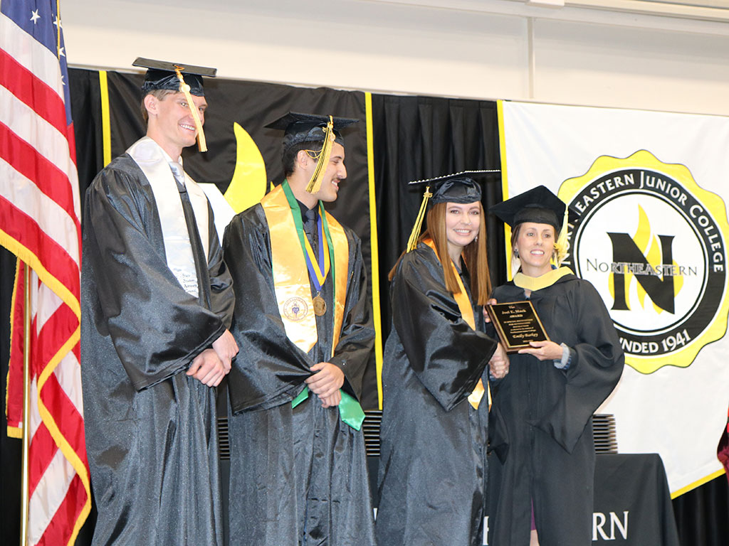 Northeastern Junior College Associated Government Second Vice President Audrey Glynn presents the Joel E. Mack Award to Emily Barkey, right, agriculture business management professor, at the commencement ceremony Friday, May 12, 2023. With them are ASG President Philip Ruch, left, and First Vice President Joao Fonseca.