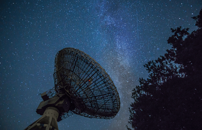 Satellite dish and a tree with the stars in the night sky